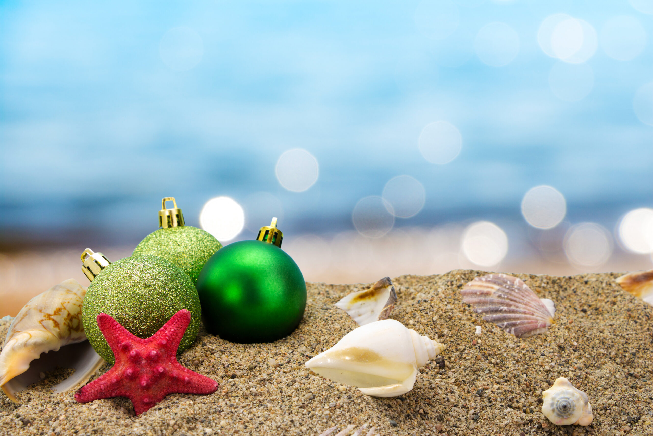 Christmas balls and shells on sand with summer sea background